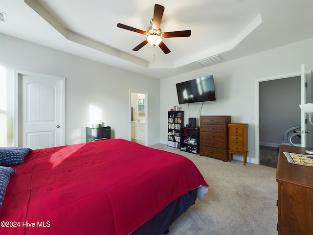 carpeted bedroom with ceiling fan, ensuite bath, multiple windows, and a tray ceiling