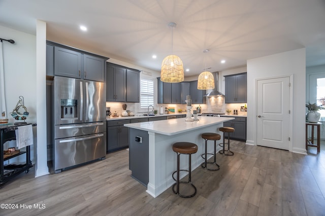 kitchen featuring wall chimney range hood, sink, stainless steel refrigerator with ice dispenser, hanging light fixtures, and a kitchen island