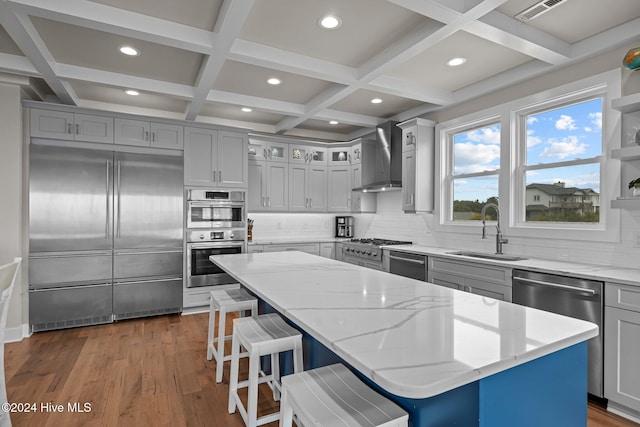 kitchen with stainless steel appliances, a kitchen island, light stone countertops, sink, and wall chimney exhaust hood