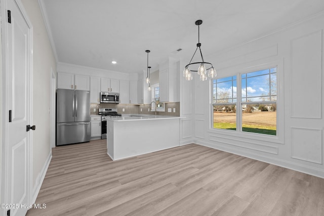 kitchen with hanging light fixtures, stainless steel appliances, kitchen peninsula, light hardwood / wood-style floors, and white cabinets