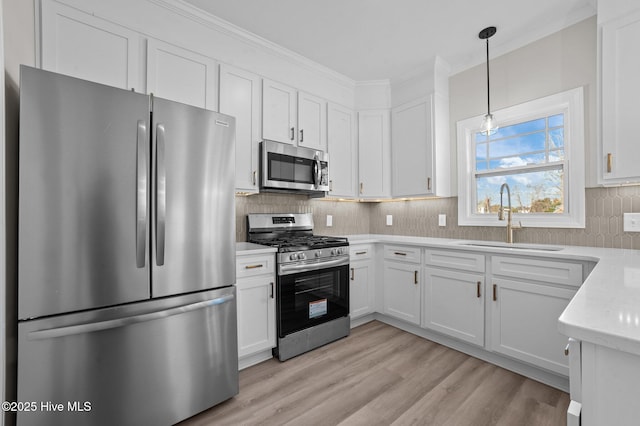 kitchen featuring appliances with stainless steel finishes, light wood-type flooring, sink, decorative light fixtures, and white cabinetry