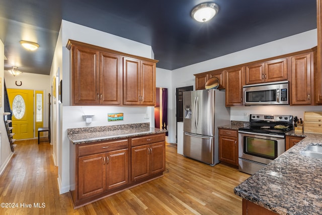 kitchen featuring stainless steel appliances, light hardwood / wood-style floors, and dark stone countertops