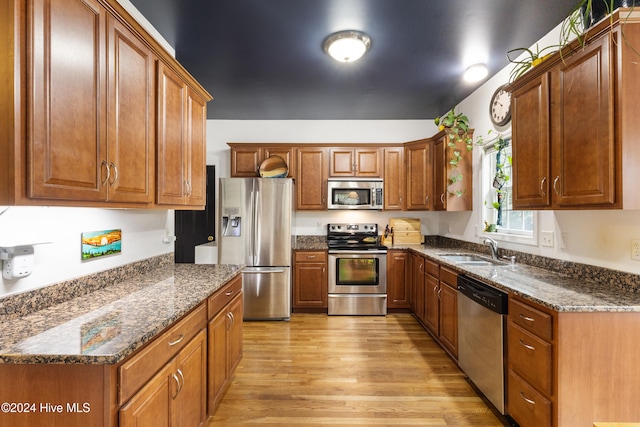 kitchen with stainless steel appliances, sink, dark stone countertops, and light hardwood / wood-style flooring