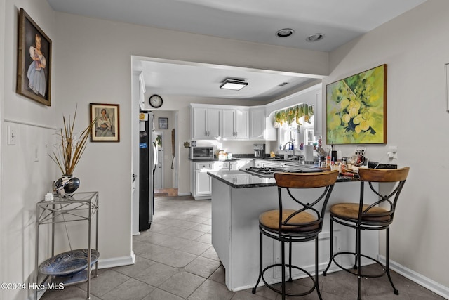 kitchen featuring stainless steel appliances, dark stone counters, white cabinetry, a kitchen breakfast bar, and kitchen peninsula