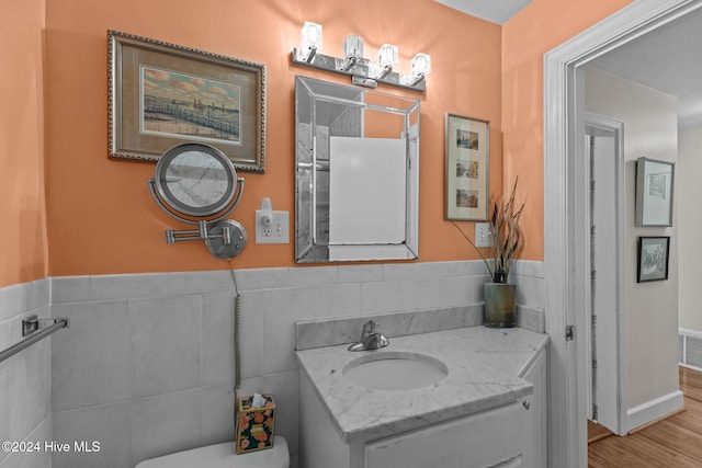 bathroom with tile walls, wood-type flooring, toilet, and vanity