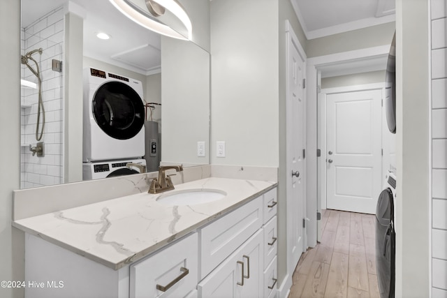 bathroom with vanity, crown molding, hardwood / wood-style flooring, a tile shower, and stacked washer / dryer