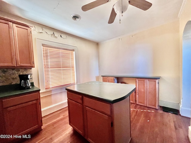 kitchen featuring hardwood / wood-style floors, a center island, backsplash, crown molding, and ceiling fan