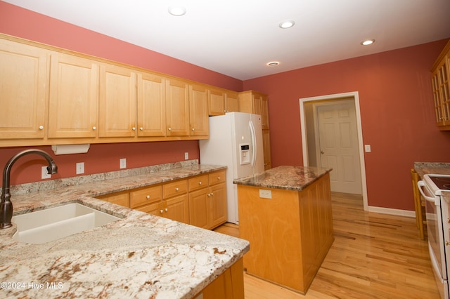 kitchen with white appliances, a center island, light stone countertops, and sink