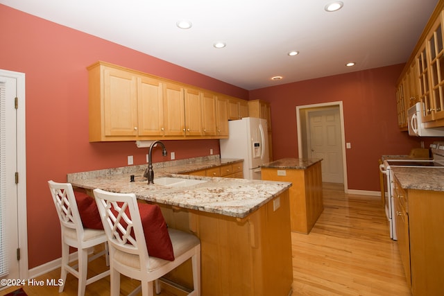 kitchen featuring light stone counters, white appliances, sink, light hardwood / wood-style floors, and a kitchen island