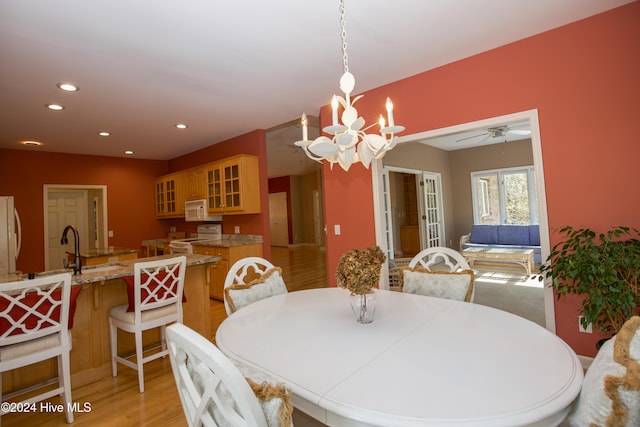 dining space with sink, ceiling fan with notable chandelier, and light wood-type flooring