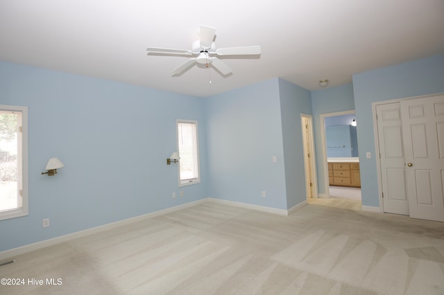 unfurnished bedroom featuring ceiling fan, light colored carpet, and connected bathroom