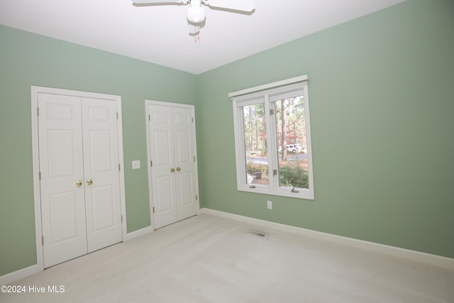 unfurnished bedroom featuring two closets, light colored carpet, and ceiling fan