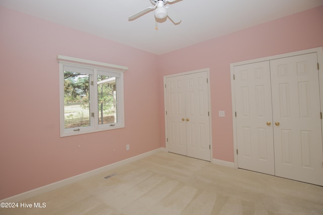 unfurnished bedroom with light carpet, ceiling fan, and two closets