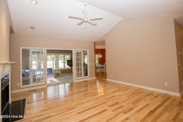 unfurnished living room featuring french doors, ceiling fan with notable chandelier, light hardwood / wood-style floors, and vaulted ceiling