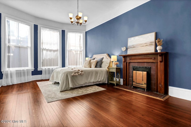 bedroom featuring dark wood-type flooring, multiple windows, a chandelier, and a tile fireplace