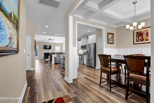 dining area with ceiling fan with notable chandelier, hardwood / wood-style floors, coffered ceiling, crown molding, and beam ceiling