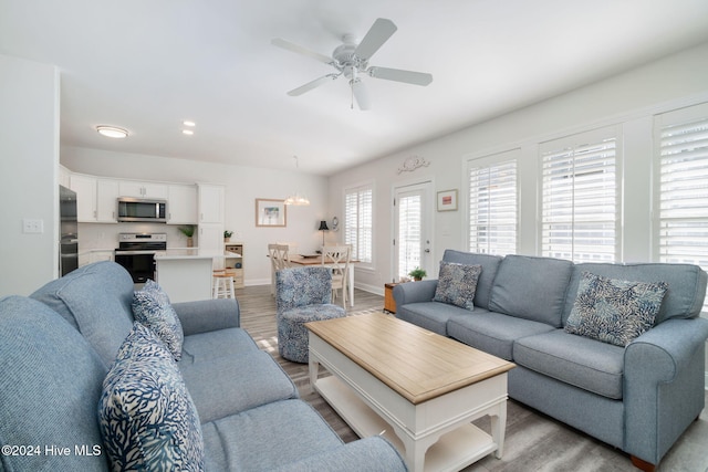 living room with ceiling fan with notable chandelier and light hardwood / wood-style floors