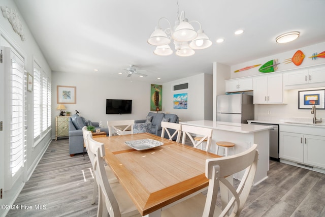 dining room with sink, ceiling fan with notable chandelier, and light wood-type flooring