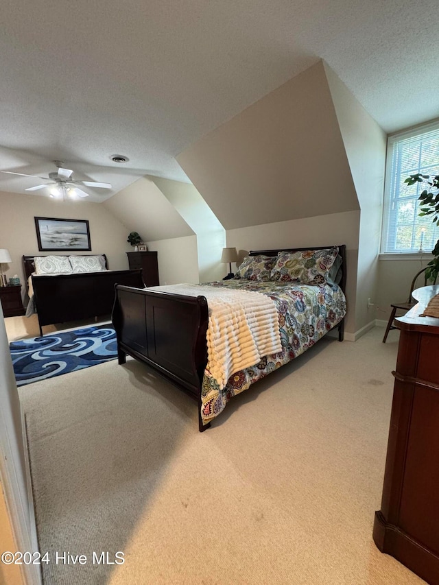 bedroom featuring lofted ceiling, a textured ceiling, light colored carpet, and ceiling fan