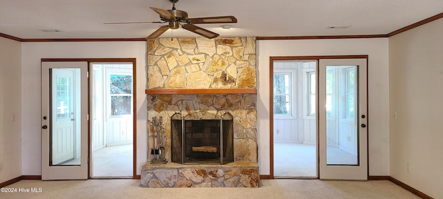 unfurnished living room with ceiling fan, a stone fireplace, crown molding, and carpet