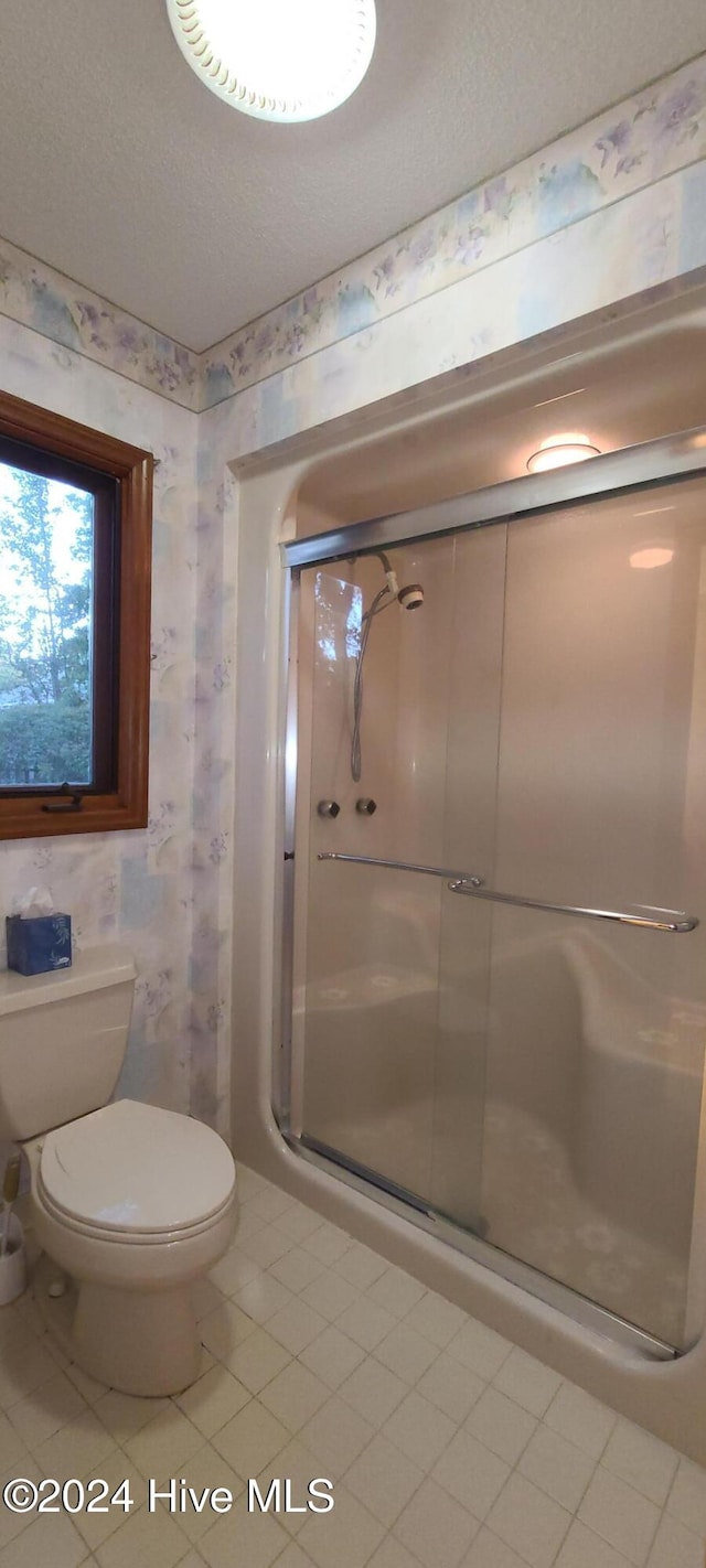 bathroom featuring toilet, tile patterned flooring, and a shower with shower door