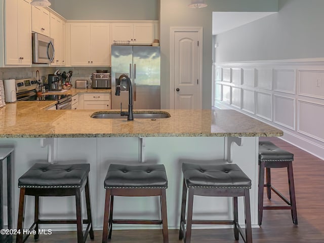 kitchen with kitchen peninsula, appliances with stainless steel finishes, a breakfast bar, dark wood-type flooring, and sink