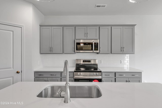 kitchen featuring gray cabinets, stainless steel appliances, and tasteful backsplash