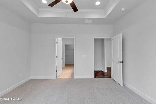 unfurnished bedroom with light colored carpet, ceiling fan, a walk in closet, and ornamental molding