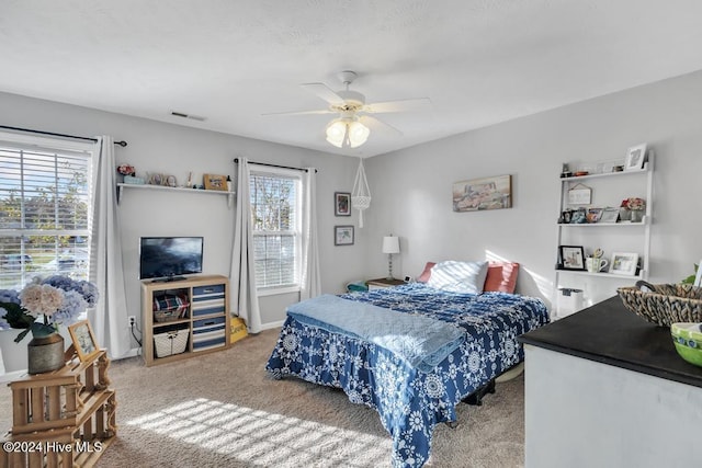 bedroom featuring ceiling fan, multiple windows, and carpet flooring