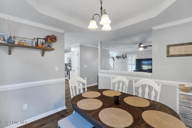 dining space featuring dark wood-type flooring, ceiling fan with notable chandelier, a raised ceiling, and ornamental molding