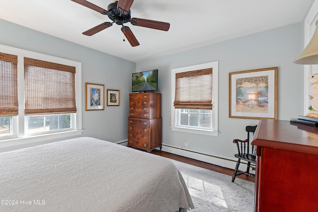 bedroom with baseboard heating, wood-type flooring, multiple windows, and ceiling fan