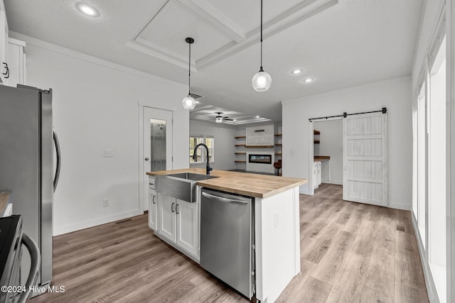 kitchen with appliances with stainless steel finishes, a barn door, a center island with sink, white cabinets, and hanging light fixtures