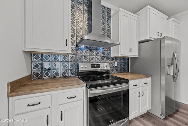 kitchen with wood counters, appliances with stainless steel finishes, wall chimney exhaust hood, white cabinets, and hardwood / wood-style floors