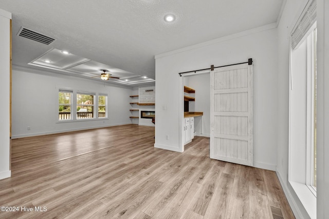 unfurnished living room featuring crown molding, light hardwood / wood-style flooring, ceiling fan, a barn door, and a textured ceiling