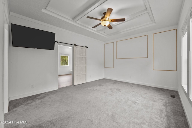 carpeted empty room featuring ceiling fan, coffered ceiling, a barn door, a tray ceiling, and ornamental molding