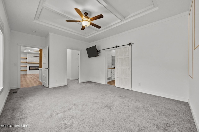 unfurnished bedroom with a walk in closet, ceiling fan, crown molding, a barn door, and carpet floors