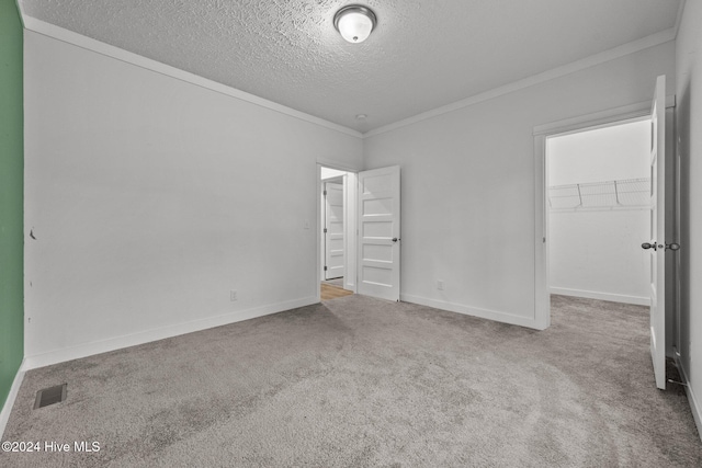 unfurnished bedroom featuring crown molding, a textured ceiling, a walk in closet, a closet, and carpet