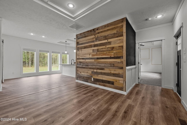 unfurnished living room featuring sink, dark hardwood / wood-style floors, crown molding, a textured ceiling, and wooden walls