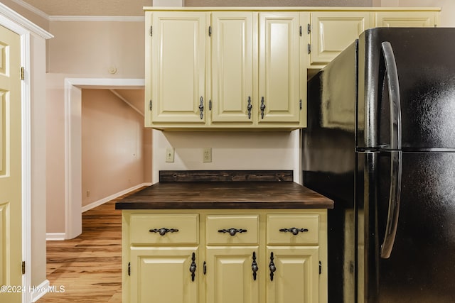 kitchen featuring black refrigerator, light wood-type flooring, ornamental molding, cream cabinets, and butcher block counters