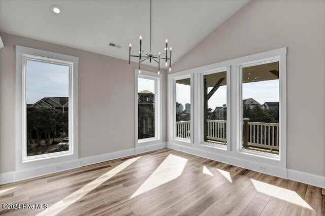 unfurnished dining area featuring light hardwood / wood-style flooring, high vaulted ceiling, and a chandelier