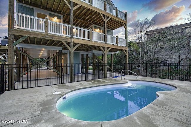 pool at dusk featuring a fenced in pool, a patio, a wooden deck, and fence