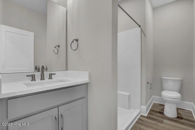 bathroom featuring vanity, wood finished floors, baseboards, a walk in shower, and toilet