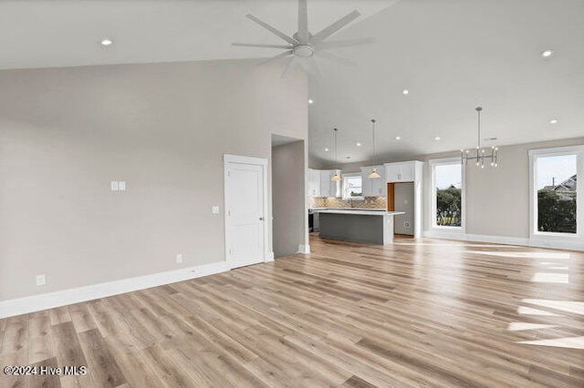 unfurnished living room featuring high vaulted ceiling, ceiling fan with notable chandelier, and light wood-type flooring