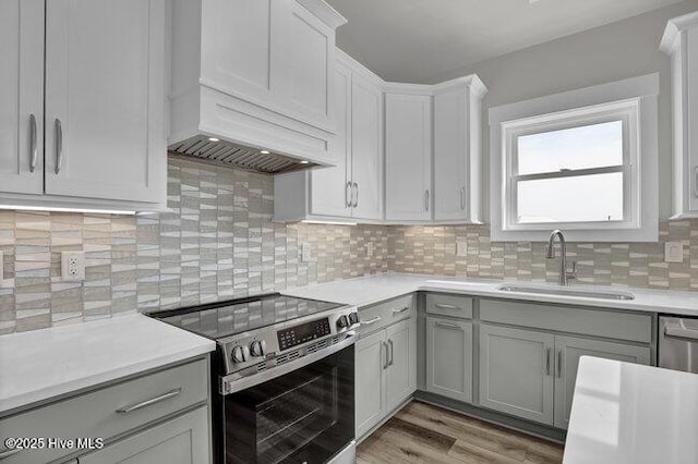 kitchen with gray cabinets, a sink, stainless steel range with electric cooktop, light countertops, and decorative backsplash