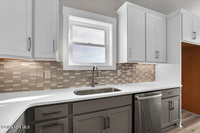 kitchen featuring gray cabinetry, sink, stainless steel dishwasher, backsplash, and light hardwood / wood-style floors