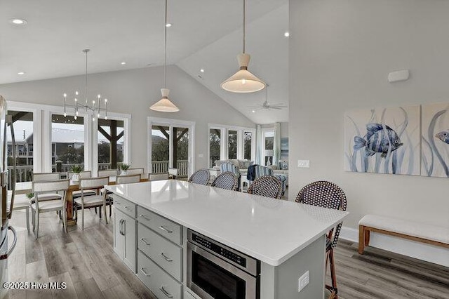 kitchen featuring light wood finished floors, built in microwave, light countertops, gray cabinets, and a kitchen breakfast bar