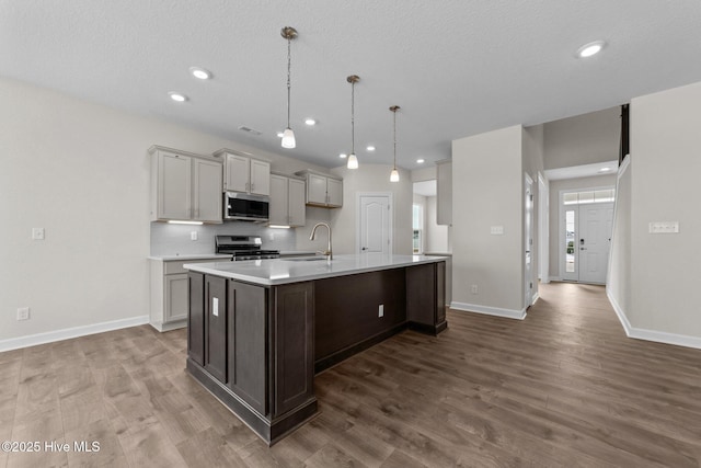 kitchen with dark wood-style flooring, appliances with stainless steel finishes, a sink, light countertops, and baseboards