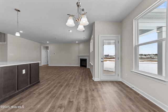 unfurnished living room featuring a textured ceiling, wood finished floors, baseboards, a notable chandelier, and a glass covered fireplace
