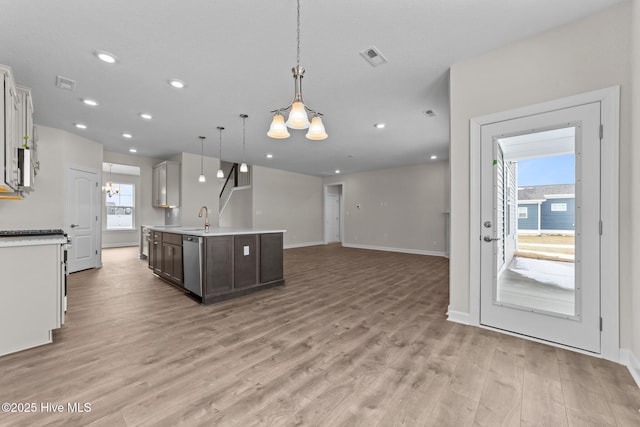 kitchen with an inviting chandelier, stainless steel dishwasher, light wood-type flooring, light countertops, and a sink