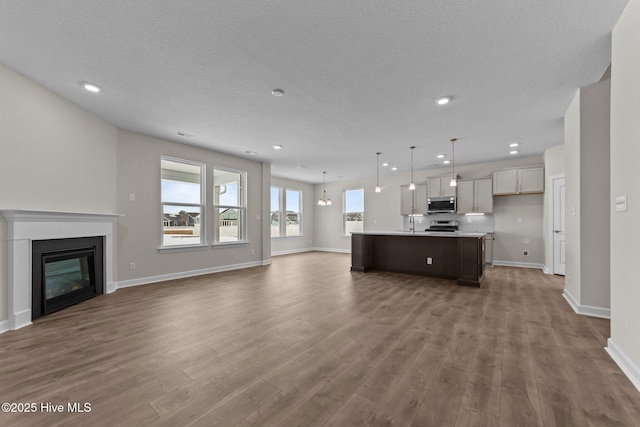 unfurnished living room featuring baseboards, a textured ceiling, recessed lighting, and wood finished floors